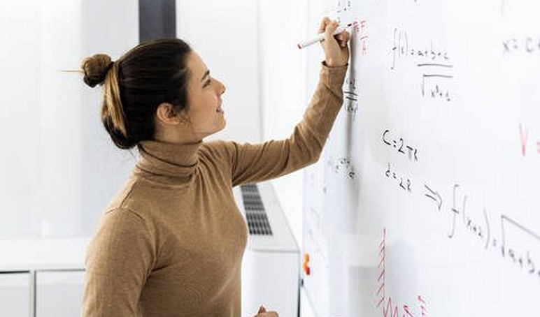 Smiling young woman solving mathematical formula on whiteboard at home GIOF10662